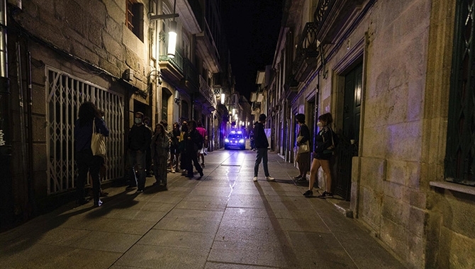 Un coche de policía pasa frente a varias personas en ambiente festivo. EP
