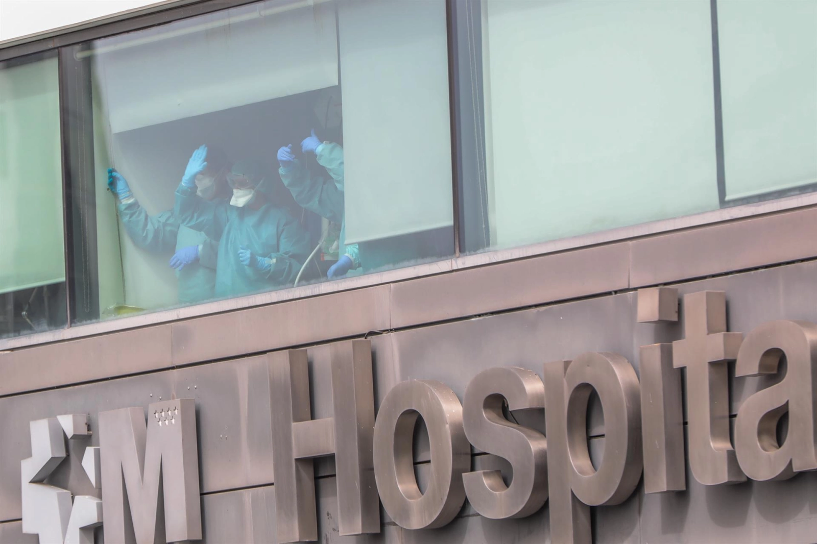 Sanitarios del Hospital de La Paz totalmente protegidos saludan y agradecen el apoyo desde una de las ventanas del centro donde se lucha contra el coronavirus / Europa Press