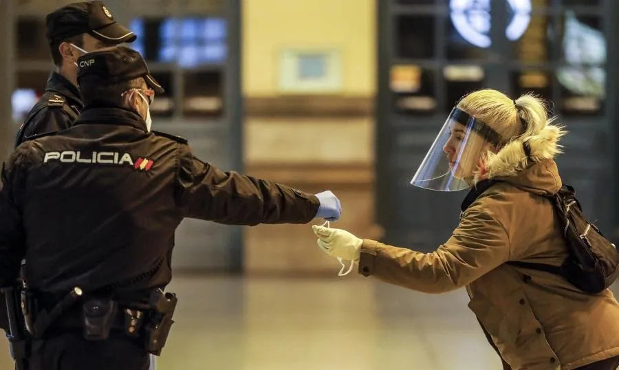 Un policía nacional entrega una mascarilla a una mujer en el vestíbulo de la estación del Norte de Valencia. Foto de Rober Solsona - EP