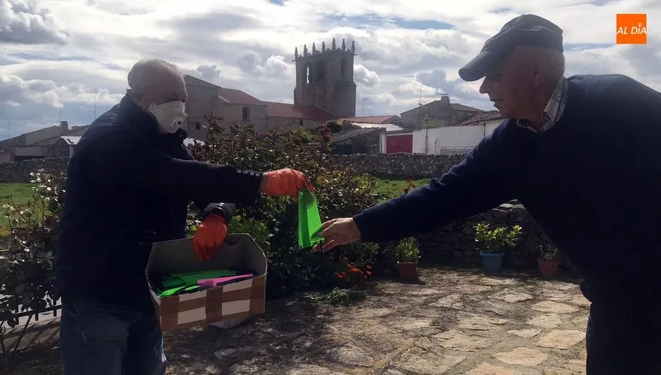 El alcalde de guadramiro, Bernabé Gil (iz.), entrega una mascarilla a un vecino