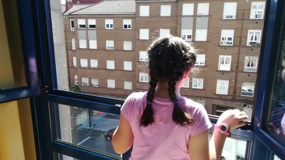 Una niña mira desde la ventana de su casa. Foto: EP