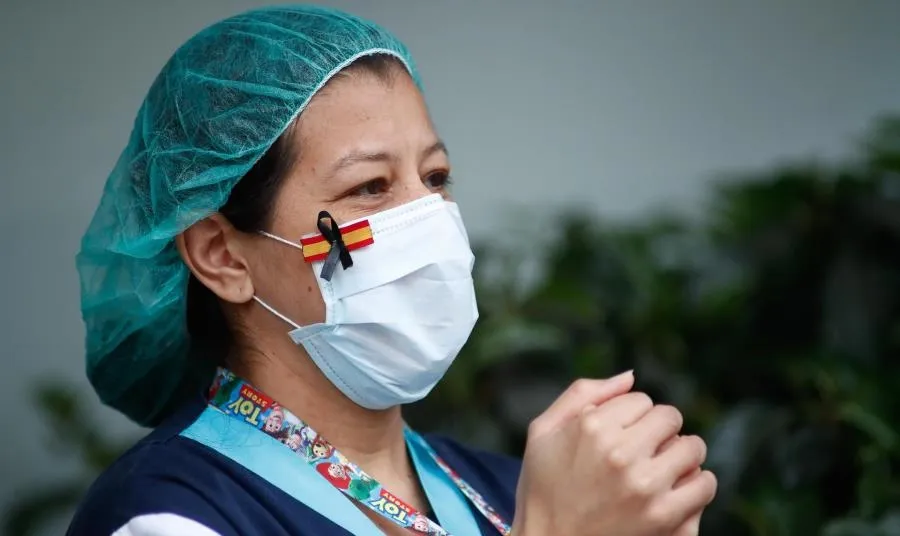 Una sanitaria, con una mascarilla que muestra una bandera de España con un lazo negro de luto por los fallecidos por coronavirus, aplaude en agradecimiento por el homenaje a los sanitarios del Hospital Fundación Jiménez Díaz en Madrid. Foto de Oscar J. Ba
