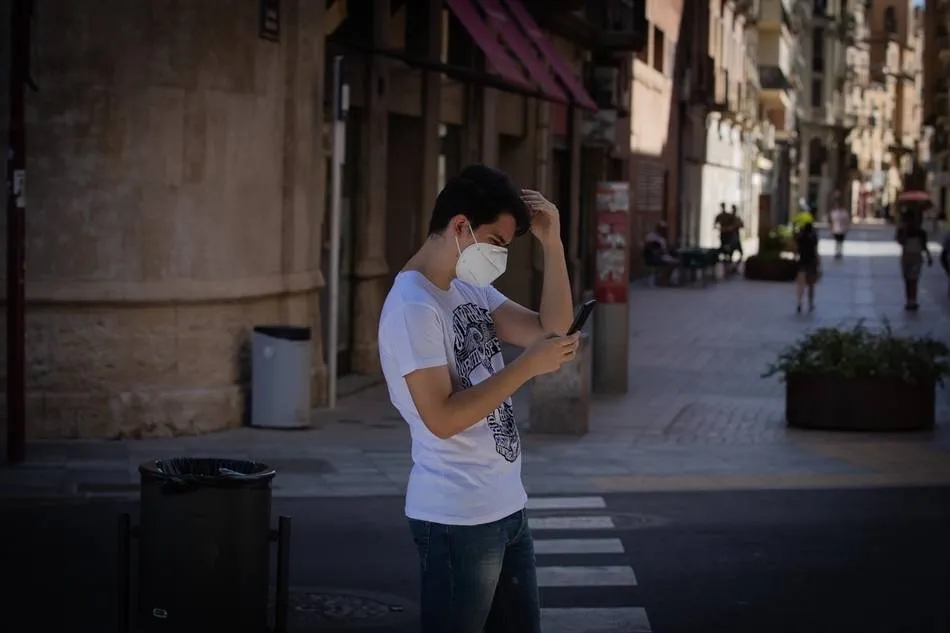 Un joven con mascarilla consulta su teléfono móvil. Foto: EP