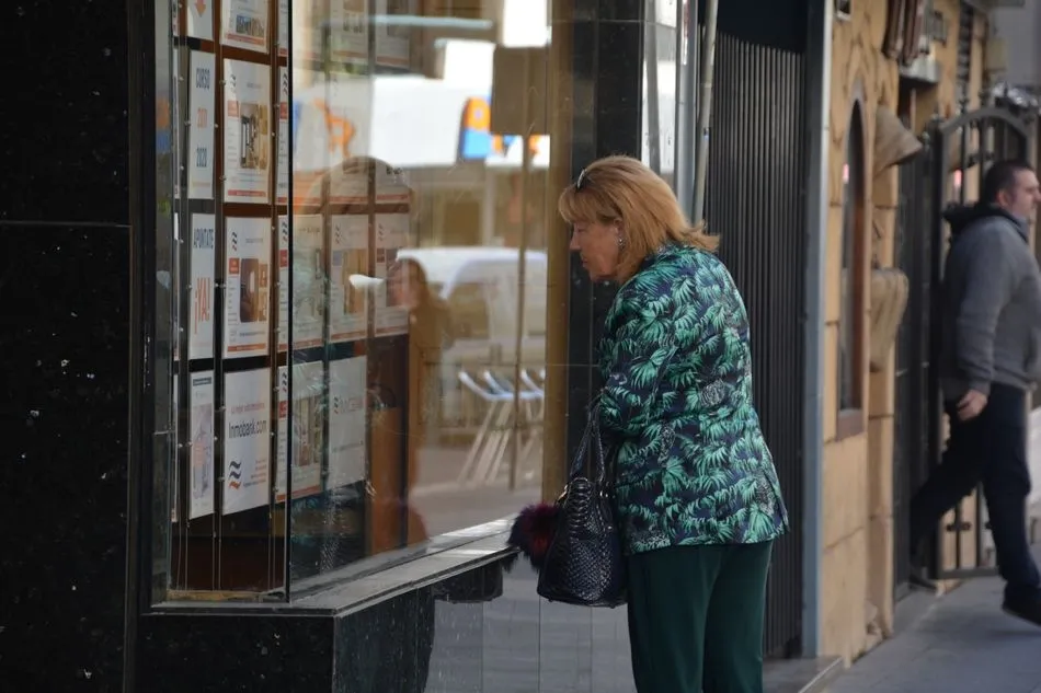 Una mujer mira los anuncios de alquiler y venta en una agencia inmobiliaria