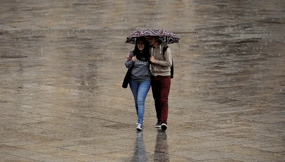 Una pareja pasea protegiendo con un paraguas de la lluvia