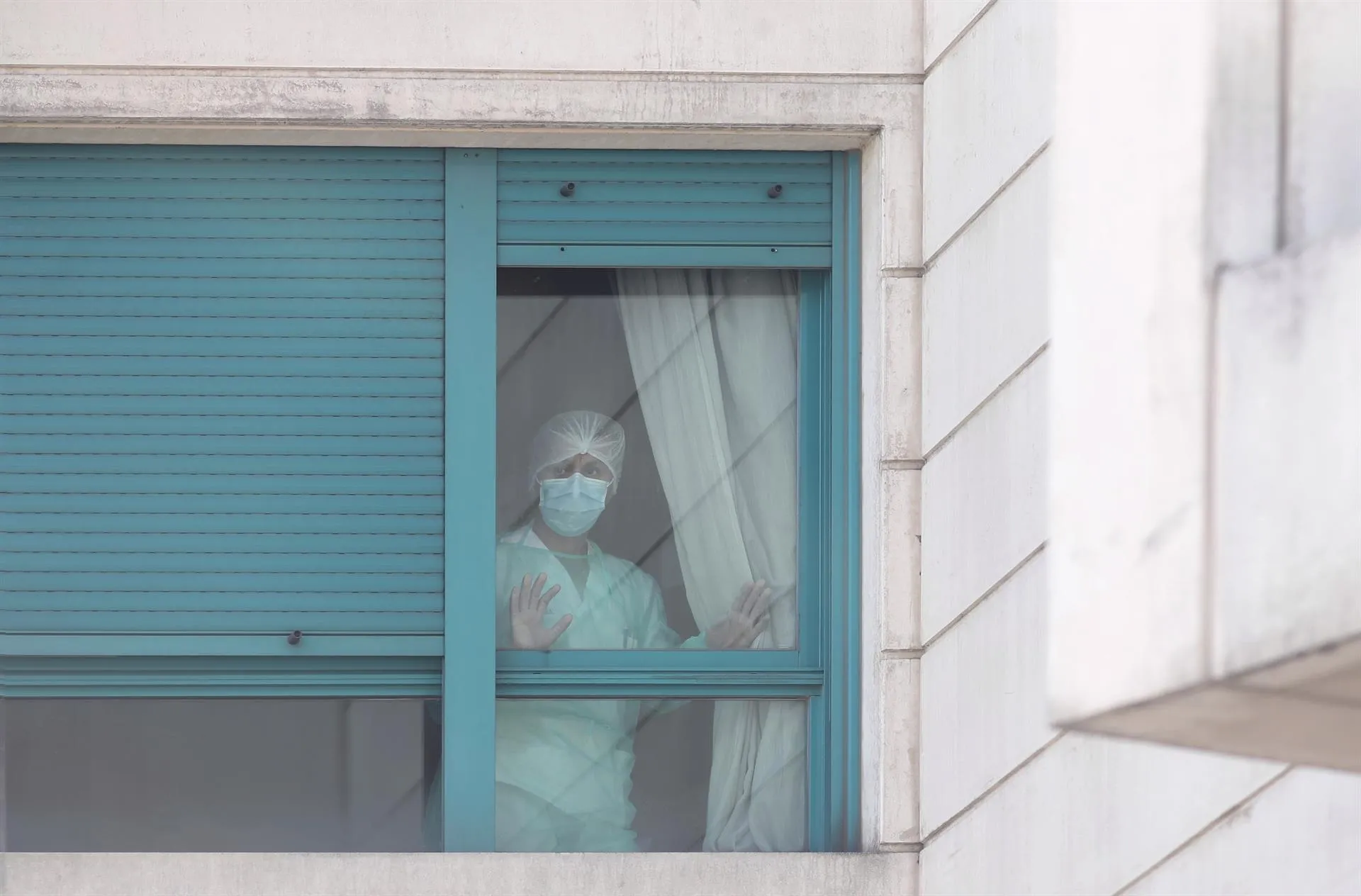 Una trabajadora del personal sanitario protegida con mascarilla se asoma por una de las ventanas de una residencia de Madrid. Foto: EP