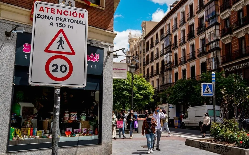 Viandantes pasan al lado de una señal que indica la limitación de la circulación a 20 km/h en una calle de Madrid. Foto A. Pérez Meca - EP
