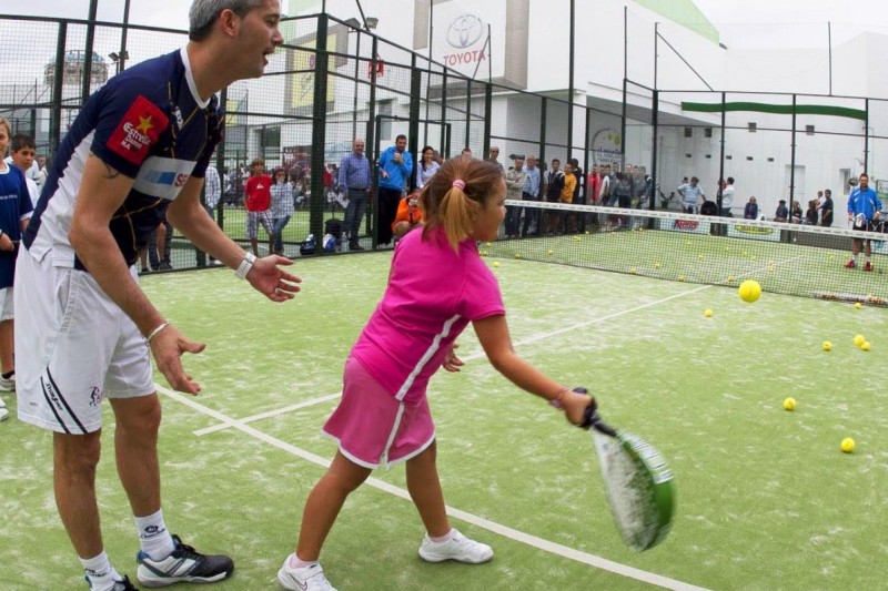 Un monitor enseña a una niña a darle a la pelota en un cancha de pádel
