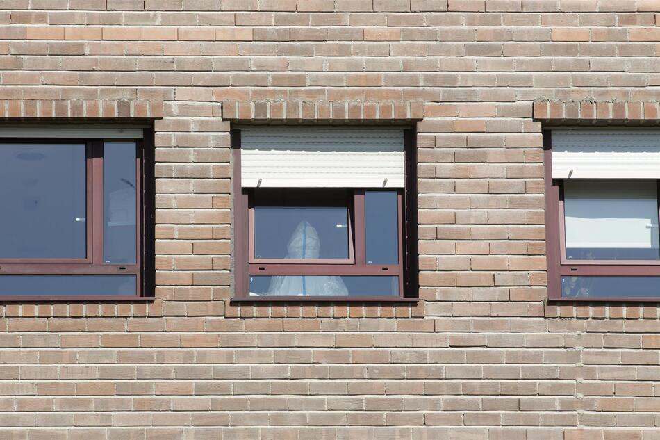 Un trabajador sanitario con un EPI en la ventana de una habitación de una residencia durante la pandemia. Foto: EP